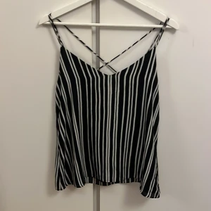 Svartvit randig linnetopp från H&M - Snygg svartvit randig linnetopp från H&M med smala axelband och korsad ryggdetalj. Perfekt för varma dagar. Toppen har en luftig passform och är tillverkad i ett lätt material.
