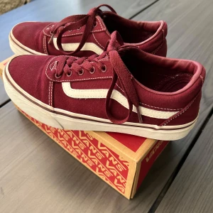 Vinröda sneakers från Vans - Snygga vinröda sneakers från Vans med klassisk vit sidosymbol och snörning. Skorna har en vit sula och är perfekta för en avslappnad stil. De kommer i originalkartong.
