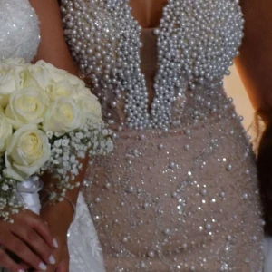 Glittrig klänning med pärlor - Elegant klänning i beige med glittrande detaljer och pärlor. Den har en djup v-ringning och en figurnära passform som framhäver silhuetten. Perfekt för speciella tillfällen. Strlk- 36,38