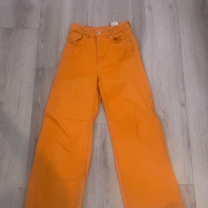 Orange byxor från H&M - Snygga orange byxor från H&M med fransiga kanter. De har en hög midja och en rak passform som ger en avslappnad look. Perfekta för att lägga till en färgklick i garderoben!