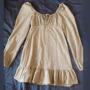 Beige klänning med volangdetalj - Charmig beige klänning med små vita prickar och volangdetalj vid fållen. 