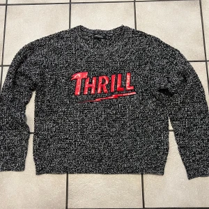 Svart och vit stickad tröja storlek M - Säljer en cool svart och vit stickad tröja från Faster Than Yesterday med röd text 'THRILL' på framsidan. Tröjan har en avslappnad passform och långa ärmar, perfekt för kyligare dagar. Hör av dig vid intresse!