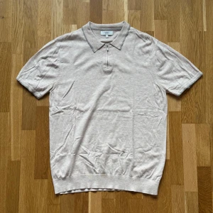 NEXT Beige Piké - Beige Piké med dragkedja istället för knappar från NEXT.  Storlek: L, Armhåla till Armhåla: 51 cm, Längd: 72 cm, Axel till Armöppning: 24 cm.  Material: 55% Cotton, 32% Nylon, 13% Lyocell. 