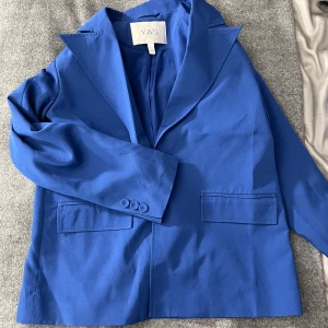 Blå kavaj från Y.A.S - Snygg blå kavaj från Y.A.S med klassisk krage och knappar vid ärmslut. Perfekt för en stilren look. Kavajen har två fickor framtill, axel puffar för en bredaxlad look och en elegant passform. Använd 1 gång. 