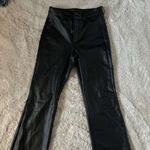 Svarta skinnbyxor - Snygga svarta skinnbyxor med hög midja och raka ben. Byxorna har en stilren design med dragkedja och knappar framtill samt fickor bak. Perfekta för en trendig look.