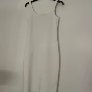 Vit ärmlös klänning - Snygg vit ärmlös klänning med smala axelband och en stilren design. Perfekt för sommarens varma dagar. Klänningen har en slits baktill för extra rörelsefrihet. Aldrig använt den 