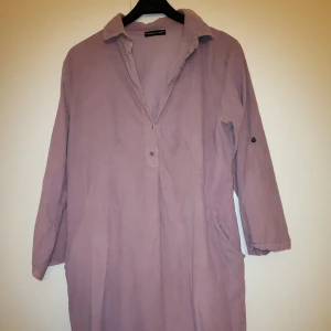 Ljuslila klänning med krage - Säljer en avslappnad ljuslila klänning med krage och trekvartsärmar. Klänningen har en knappdetalj framtill och är perfekt för en bekväm och stilren look. Passar bra till både vardag och speciella tillfällen. Sydd i ett tunt manchestertyg. 