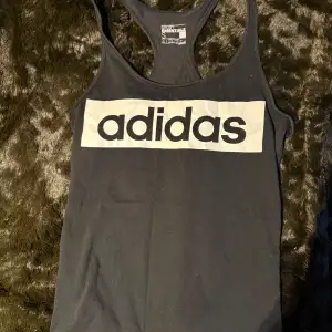 Säljer en svart linnetopp från Adidas med stort vitt logotryck på framsidan. Perfekt för träning 