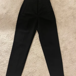 Svarta kostymbyxor från Zara - Snygga svarta kostymbyxor från Zara i en elegant design. Byxorna har en hög midja och raka ben, perfekta för en stilren look. I croppad stil och perfekt till kontoret eller skolan.