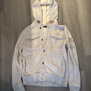 Polo Jeans Ralph lauren huv tröja - Tjabba! Säljer en grå huvtröja från Polo Jeans Co. med broderad logga på ärmen. Tröjan har knappar framtill, två bröstfickor och ribbade muddar. Perfekt för en avslappnad stil. Skriv vid någon som helst fundering💯🤝