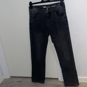 Mörk gråa jeansbyxor från LAB Industries  - Snygga svarta jeansbyxor från LAB Industries med en klassisk femficksdesign. Byxorna har en knapp och dragkedja framtill och är perfekta för en stilren look. De har en rak passform och är tillverkade i ett slitstarkt material. I regular fit i storlek 164 som passar 172