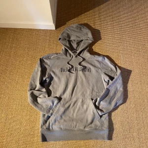 Grå hoodie från Helmut Lang - Säljer en stilren grå hoodie från Helmut Lang med broderad logga på bröstet. Tröjan har en klassisk design med huva och långa ärmar, perfekt för en avslappnad look. Kom med frågor och funderingar! Ej fast pris!