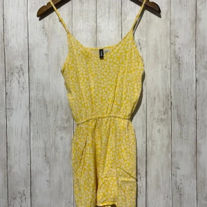 Gul blommig jumpsuit från H&M - Söt gul jumpsuit från H&M med blommigt mönster. Den har smala axelband och en avslappnad passform, perfekt för varma dagar. Jumpsuiten är i ett lätt och luftigt material.💖✨