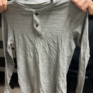 Grå långärmad tröja med knappar - Säljer en stilren grå långärmad tröja med två knappar vid halsen. Perfekt för en avslappnad look. Tröjan är i ett mjukt material som känns skönt mot huden.