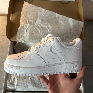 Nike Air Force 1 - Säljer ett par klassiska vita Nike Air Force sneakers. Skorna har en stilren design med snörning och perforerade detaljer på ovansidan för ventilation. Perfekta för en casual look.