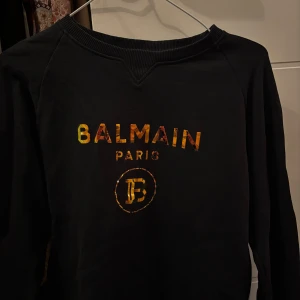 Svart tröja från Balmain - Tröjan är självklart äkta men några år gammal dock så är den 2-3 gånger så jag inte riktigt tyckt den passar min stil. Snygg svart tröja från Balmain med färgglatt tryck på framsidan. Perfekt för en stilren look med en touch av lyx. Tröjan har långa ärmar och är tillverkad i bomull för en bekväm passform.