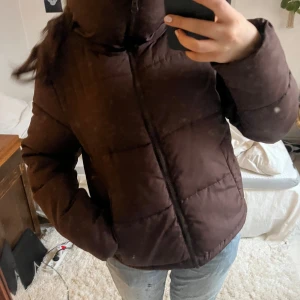 Brun pufferjacka från Bik Bok - Säljer en brun pufferjacka från Bik Bok i storlek XS. Jackan har en dragkedja framtill och är perfekt för kyligare dagar. Den är quiltad och har långa ärmar för extra värme. Gjord av återvunnet material.