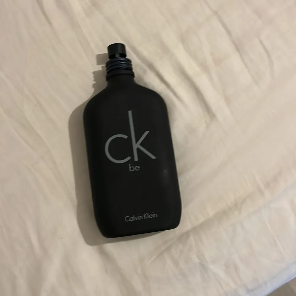 Säljer en stilren CK Be parfym från Calvin Klein. Flaskan är svart och har en minimalistisk design med märkets logga i grått. Perfekt för den som gillar en fräsch och diskret doft. Flaskan har en praktisk skruvkork.. Perfume.