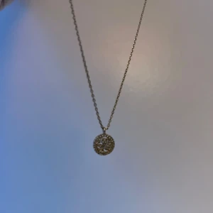 Guldhalsband med rund hängsmycke - Elegant guldhalsband med ett runt hängsmycke. Hängsmycket har ett intrikat mönster som ger en stilren och tidlös look. Perfekt för att komplettera din outfit med en touch av elegans.