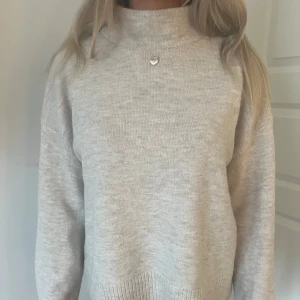 Beige stickad tröja - Säljer en stilren beige stickad tröja med hög krage. Tröjan har långa ärmar och en mjuk, bekväm passform. Perfekt för kyligare dagar och enkel att matcha med olika outfits.