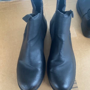 Svarta chelsea boots - Snygga svarta chelsea boots i skinn med elastiska paneler på sidorna för enkel på- och avtagning. Perfekta för både vardag och mer uppklädda tillfällen. Storlek 41.