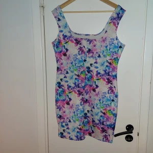 Blommig klänning från NLY One - Säljer en färgglad blommig klänning från NLY One i storlek XL. Klänningen har en ärmlös design och en bekväm passform, perfekt för sommarens varma dagar. Den har ett vackert mönster i olika nyanser av blått, rosa och grönt.