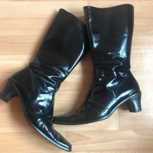 Svarta stövlar med klack - Snygga svarta stövlar i syntetmaterial med dragkedja på sidan och en elegant klack. Perfekta för en stilren look. Italienska och passar 38-39 