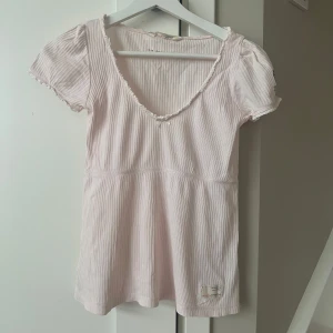 Ljusrosa ribbad topp Odd Molly - Säljer en söt ljusrosa ribbad topp från Odd Molly. Toppen har korta ärmar och en v-ringad hals med spetsdetaljer. Den har också en liten rosett framtill och ett tryck på ärmen. Knappt använd. 