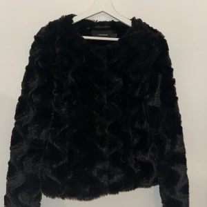 Svart pälsjacka från Vero Moda - Snygg svart pälsjacka från Vero Moda i storlek S. Jackan har en fluffig och mjuk textur, perfekt för att hålla dig varm och stilren under kyliga dagar. Den har långa ärmar och en klassisk passform.