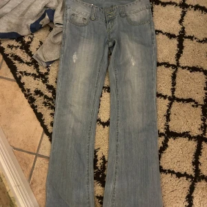 Blå bootcut jeans - Snygga blå bootcut jeans med slitningar framtill. Klassisk femficksdesign och dekorativa nitar på bakfickorna. Perfekta för en avslappnad stil. Midjemått cirka 38 och innerben cirka 80