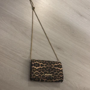 Leopardmönstrad axelväska med kedja - Snygg leopardmönstrad axelväska med guldfärgad kedja. Perfekt för att ge din outfit en trendig touch. Väskan har en stilren design och är lätt att bära med sig. Pris kan diskuteras