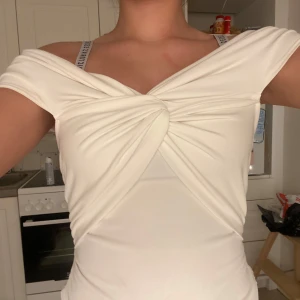 Vit offshoulder topp - Snygg vit offshoulder topp med knutdetalj framtill. Perfekt för en stilren look. Toppen har en åtsittande passform och är tillverkad i ett mjukt material.