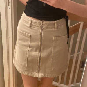 Beige jeanskjol från Gina Tricot - Beige medellång jeanskjol med fickor framtill och dragkedja. Så gott som ny!