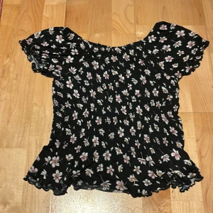 Blommig topp från Lindex  - Söt blommig topp från Lindex  i svart med vita och rosa blommor. Toppen har korta ärmar och en elastisk passform som ger en bekväm känsla. Perfekt för sommarens äventyr!