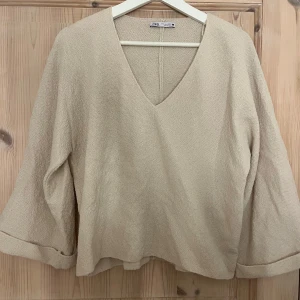 Beige tröja från Zara - Säljer en stilren beige tröja från Zara med v-ringning och långa ärmar. Tröjan har en mjuk och bekväm textur, perfekt för en avslappnad look. Passar bra till både jeans och kjol.