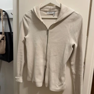 Beige ribbad hoodie från Weekday - Säljer en stilren beige hoodie från Weekday i ribbat material. Den har en dragkedja framtill och långa ärmar. Perfekt för en avslappnad look.