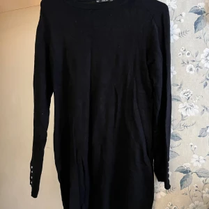 Svart långärmad klänning från Zara - Snygg svart långärmad klänning från Zara med dekorativa knappar på ärmarna. Perfekt för en stilren look. Tröjan är i ett mjukt material som ger en bekväm passform.