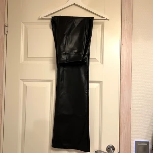 Svarta skinnbyxor från Madlady - Snygga svarta skinnbyxor från Madlady i storlek S. Byxorna har en tight passform och är perfekta för en trendig look. De har en knappdetalj i midjan och är tillverkade i ett syntetiskt material som ger en cool läderlook. Helt nya!