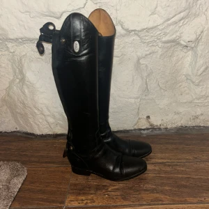 Svarta ridstövlar med dragkedja - Snygga svarta ridstövlar i skinn med dragkedja baktill. Perfekta för ridning och har en klassisk design med rundad tå och låg klack. Från crw, se slitningarna på näst sista bilden 