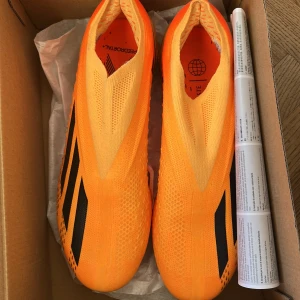 Adidas X Crazyfast.1 FG Fotbollsskor - Säljer ett par Adidas X Crazyfast.1 FG fotbollsskor i en iögonfallande orange färg med svarta detaljer. Skorna har en lätt och strömlinjeformad design med FG-dobbar för optimalt grepp på gräsplaner. Perfekta för snabba spelare som vill dominera på planen.