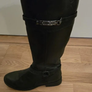 Svarta stövlar med spänne - Snygga svarta stövlar i skinn med dekorativt spänne och dragkedja på sidan. Perfekta för höst och vinter. Används ett par gånger med i väldigt bra skick. 💕Du står för frakten !