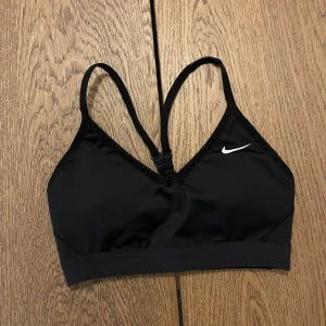 Svart sporttopp från Nike - Säljer en svart sporttopp från Nike med smala axelband och en liten vit logga på framsidan. Toppen har en enkel design och är perfekt för träning.