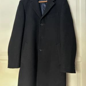 Svart Stilren Rock - Elegant svart Rock med klassisk design och knappar framtill. Strl 46 vilket motsvarar S-M. Perfekt för kyligare dagar med sin stilrena look och långa ärmar. Fraktar gärna, finns och hämta i Bollebygd annars.                            Hör av er vid frågor!