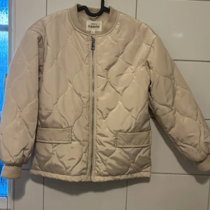 Barnstorlek: Beige quiltad jacka från KappAhl - Storlek 134. Säljer en snygg beige quiltad jacka från KappAhl. Jackan har en dragkedja framtill och reflex i ryggen. Använd endast ett fåtal gånger. 