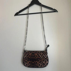 Leopardmönstrad axelväska från Bershka - Snygg leopardmönstrad axelväska från Bershka med kedjerem och dragkedja. Perfekt för att ge din outfit en trendig touch. Väskan är kompakt och lätt att bära med sig.