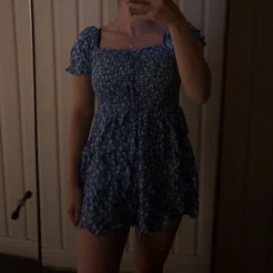 Blå blommig klänning - Säljer denna klänningen som är köpt på new yorker förra sommaren då jag inte använt den! Prislappen sitter fof på. Storlek S men passar dig som har storlek XS också! Den har shorts i sig så som en bodysuit/jumpsuit