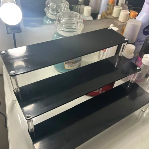 Svart sminkhylla - Praktisk och stilren svart sminkhylla med tre nivåer, perfekt för att organisera dina skönhetsprodukter. passar utmärkt på sminkbordet.