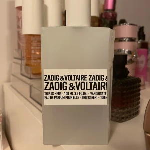 Zadig & Voltaire This Is Her Eau de Parfum 100ml - Zadig & Voltaire This Is Her är en Eau de Parfum i en stilren vit flaska på 100 ml. Doften är modern och chic, perfekt för den som vill ha något unikt och sofistikerat. Flaskan har en minimalistisk design med svart text, vilket ger en cool och trendig känsla. Det är ungefär 60 ml kvar i flaskan och jag säljer den då den inte kommer till användning.