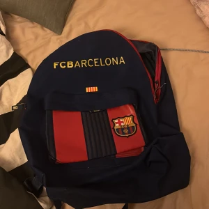 Blå och röd FC Barcelona ryggsäck - Snygg ryggsäck i blått och rött med FC Barcelona-logga. Perfekt för fans av laget. Ryggsäcken har justerbara axelremmar och en praktisk dragkedja för enkel åtkomst.