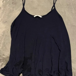 Marinblått linne från Ellos - Snygg marinblått linnetopp från Ellos med smala axelband och v-ringning. Perfekt för varma dagar då det är ett väldigt luftigt linne. Enkel och stilren design som passar till det mesta. Säljer då de inte kommer till användning.